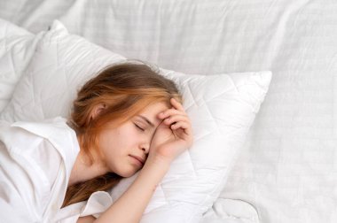 Genç kız yatakta uyuyor, beyaz yastık ve yatak, sağlıklı yaşam tarzı, dinlenme ve bencillik, iyi uyku konsepti, asgari nötr beyaz yatak odası İskandinav tarzı.