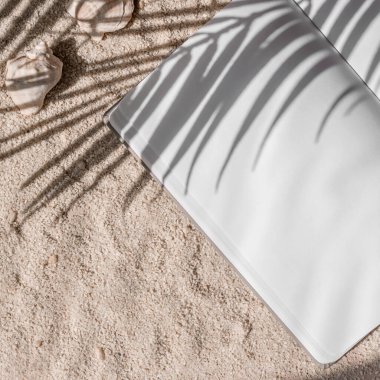 Kum zemininde, palmiye yaprakları, güneş ışığı gölgesi ve estetik yaz modeli olan boş kâğıt defter kağıdı..