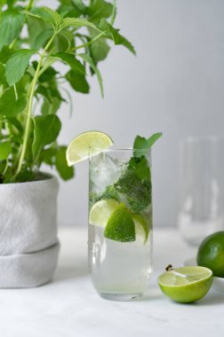 Taze buzlu mojito kokteyli, limon, nane ve buzlu uzun bardakta, nane şekeri ve mermer masada yeşil limon, ev yapımı yaz içeceği..