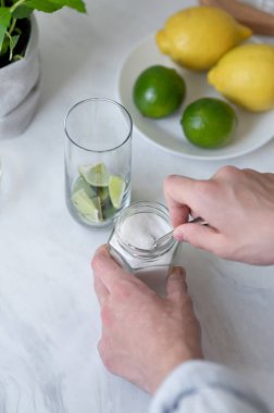 Ev yapımı mojito kokteyli hazırlama süreci, şekeri nane ve limonla bardağa koyan kişi, mojito tarifi için malzemeler.