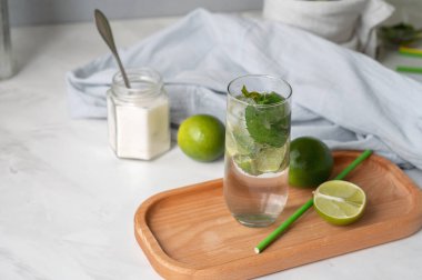 Buzlu mojito ferahlatıcı içecek, yeşil limon, beyaz masada şeker, yazlık ev yapımı taze içecek..