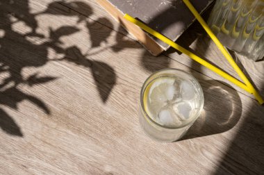 Kahverengi ahşap masa arkasında limon ve buzla doldurulmuş su içeceği. Doğal güneş ışığı gölgeleri, boş fotokopi alanı, sağlıklı yaz yaşam tarzı kavramı..