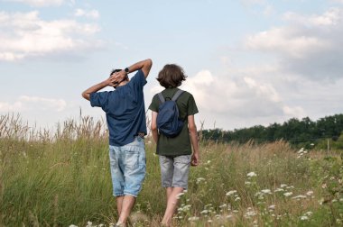 Aile kırsalda yürüyüş yapıyor, baba ve genç oğlu güzel çiçeklerle çayırlarda yürüyor, yaz günü bulutlu mavi gökyüzü..