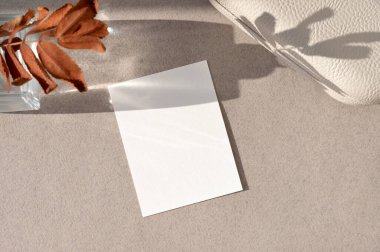 Boş beyaz desenli kağıt kartın, doğal güneş ışığı gölgeleriyle soyut estetik çiçekli ve kahverengi yapraklı nötr toprak masa zemininin bir kopyası. Düğün davetiyesi şablonu, kartpostal