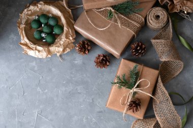 Kahverengi, çam ağacı dallarıyla süslenmiş Noel hediyesi kutuları ve gri masa arkasında koni..