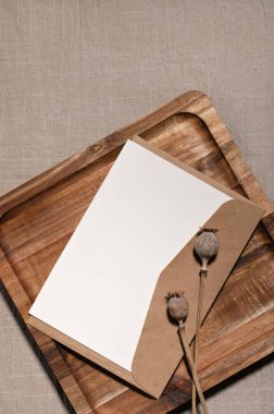 Estetik kartpostal, mektup ya da düğün davetiyesi tasarım şablonu, boş kağıt maketi, zarf, kahverengi ahşap tepside haşhaş çiçekleri, nötr kahverengi keten kumaş arka plan.