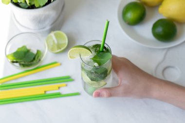 Taze yaz içeceği yeşil ve sarı limonlu mutfak masasında, nane ve içme pipetleri, buzlu mojito kokteyli ile el ele tutuşan bardak, yaşam tarzı.