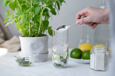 Ev yapımı mojito kokteyli hazırlama süreci, taze malzemeli ev mutfağı, limon, nane, şeker. Kireç ve nane ile bardağa şeker dök..