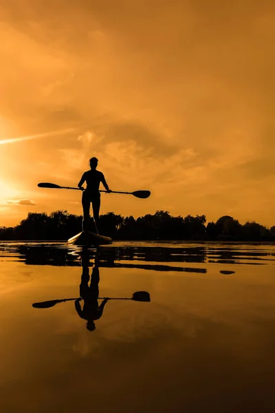 Woman on sup board, paddle boarding at sunset reflection on water