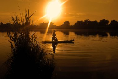 Yemek masasında bir kadın, gün batımında sörf yaparken suda yansıyor.