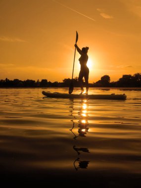 Yemek masasında bir kadın, gün batımında sörf yaparken suda yansıyor.