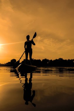 Yemek masasında bir kadın, gün batımında sörf yaparken suda yansıyor.