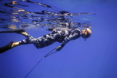 Mızraklı balıkçı denizin yüzeyinde yüzüyor, zıpkınla balık avlıyor