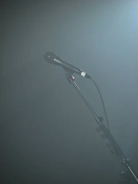 白い光が霧の中を流れるスタンドに有線歌手のマイク スタンドにはギターピックがある — ストック写真
