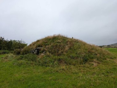Kırsal alandaki tarihi bir yerin yakınındaki kapalı bir günde çimenli bir tarlaya antik bir mezar yığını.