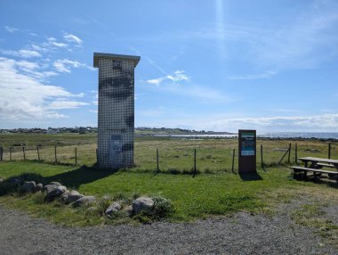 Sakin gökyüzü ve kıyıya yakın yeşil tarlaları olan sakin bir manzaraya bakan manzara.