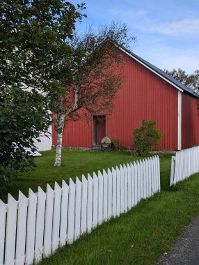 Kırsalda beyaz çitleri olan kırmızı ahşap bir ahır.