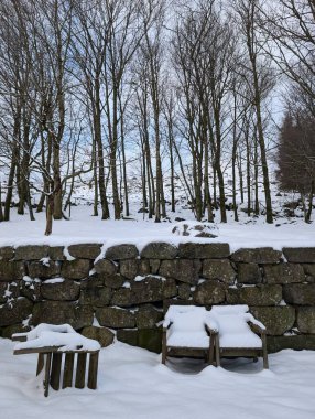Kışın taş duvarda karla kaplı iki ahşap sandalye. 