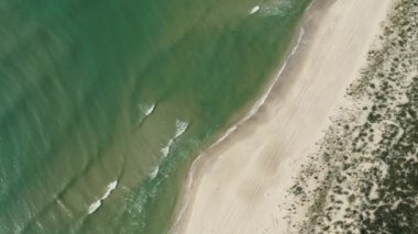 Güneşli bir yaz gününde okyanus kıyısında uçan bir kuşun havadan görünüşü. Gelen dalgalar tekrar tekrar kumlu tropikal kıyılara çarpıyor..