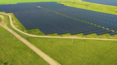 Gün batımında güneşten enerji alan sıra sıra güneş panelleri olan bir güneş paneli manzarası. Geniş bir alana yerleştirilmiş güneş panelleri.