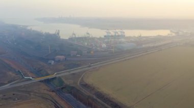 Sabah sisinde körfezin kıyısındaki kargo limanının hava görüntüsü. Konteynırlar, vinçler, demiryolları, kamyonlar, körfezin kıyısındaki limandaki gemiler. Sanayi manzarası.