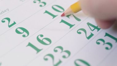 Person marking important dates on the calendar with a red pencil. Planning important business meetings and events. Close up 4k footage.
