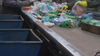 Three workers sorting plastic bottles in a recycling factory. Factory labourers sorting plastic bottles as they move on a conveyor belt in a recycling plant. Incredible slow-motion footage.