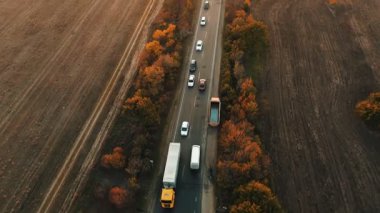 Sonbahar günbatımında otoyol boyunca giden arabaların hava görüntüsü. Arabalar kırsal yol boyunca bir araba akışında ilerlerken akşam tarlalarla çevrilidir..