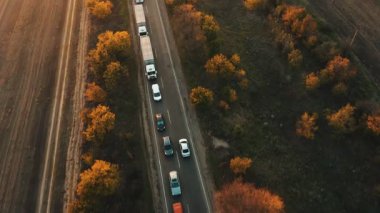 Akşamları tarlalarla çevrili bir gece yolundaki trafik sıkışıklığının hava görüntüsü. Sonbahar günbatımında otoyolda giden arabalar.