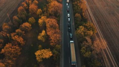 Akşamları çevresi tarlalarla çevrili bir banliyö yolundaki trafik sıkışıklığının hava görüntüsü. Sonbahar günbatımında otoyolda giden arabalar.