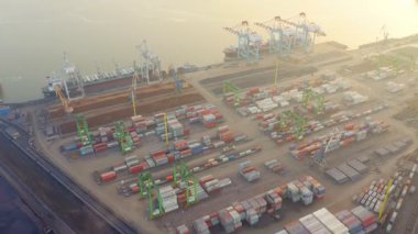 Güneşli bir yaz akşamında kargo limanının havadan görüntüsü. Liman yükleme alanında konteynırlar, kargolar, vinçler, kamyonlar var. Akşam endüstriyel manzara gün batımında.