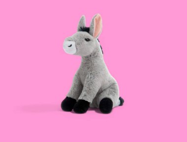 Pembe arka planda oturan yumuşak peluş oyuncak eşek.