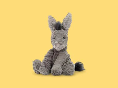 Sarı arka planda oturan komik, küçük, yumuşak peluş oyuncak.