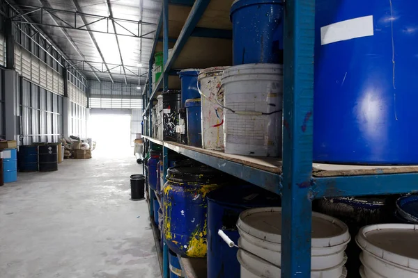 Photographs of used paint and chemical drums placed on shelves in a warehouse hallway with open doors and lighting.