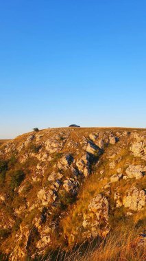Kayalık dağın tepesinde çimenli ve mavi gökyüzü olan siyah arabalı gün batımı manzarası. Cheile Tureniului, Cluj, Romanya