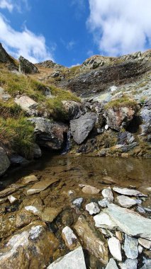 Güneşli bir yaz gününde Carbunele Şelalesinin dibinde. Kayalık dağdaki yeşil çimenler. Mavi gökyüzünde beyaz bulutlar. Transalpina Yolu, Valcea, Romanya