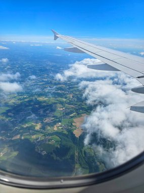 Güneşli bir günde bir uçağın penceresinden beyaz bulutların arasından Alman kırsalları görülür. Düsseldorf, Almanya