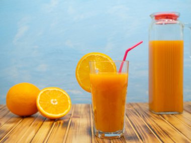 Natural orange juice in a jug on a wooden table on a blue background.