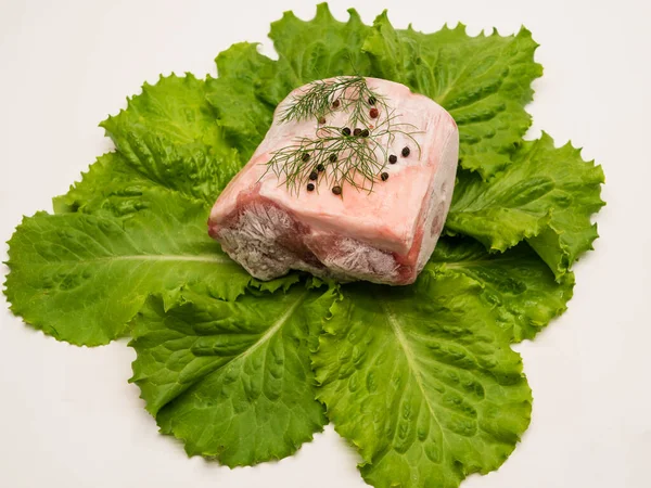 Piece of frozen meat, from which blows frosty freshness and cold. The meat lies on the leaves of fresh, green lettuce. Close-up