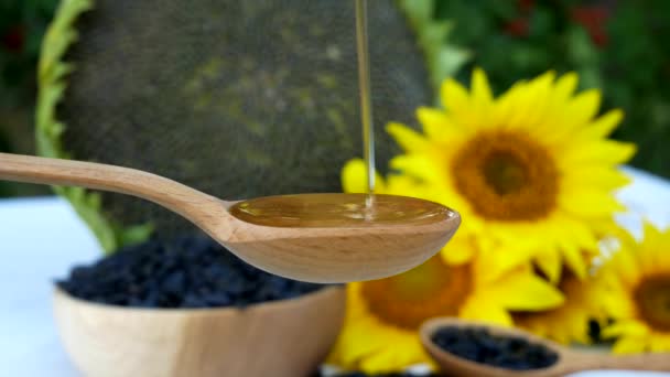 在黄色花朵和向日葵的衬托下 将液体向日葵油倒入勺子 旁边放满了种子的木制碗 — 图库视频影像