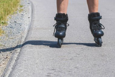 Legs of woman who is learning of inline skating on asphalt road