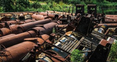 Rusty metal scrapyard on the bank of water reservoir. Remains of metal containers and raft