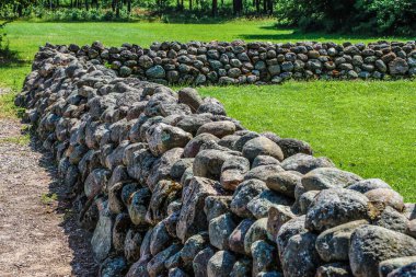 Çimlerin arasındaki eski, kuru taş duvarın köşesinde.