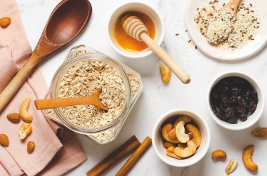 Ev yapımı tahıl gevreği. Fındıklı yulaf ezmesi, tohumlar, tarçın çubukları ve ballı beyaz mermer arka plan, üst manzara.