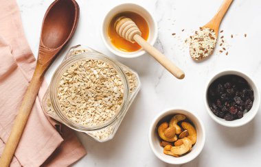 Yulaf ezmesi, bal, fındık ve kuru kızılcık beyaz mermer arka planda.