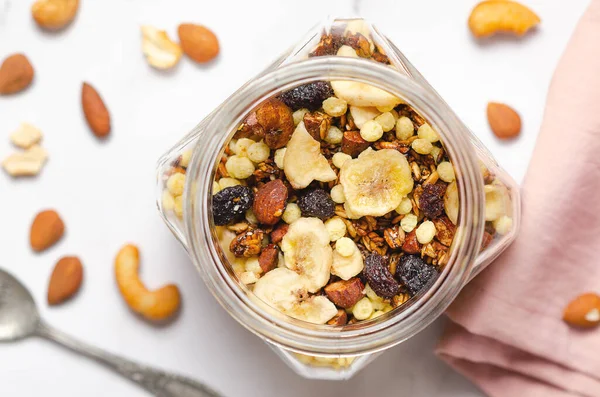 stock image Homemade granola with dried banana slices, dried cranberries and nuts in a glass jar, top view.