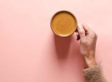 Pembe arka planda bir fincan kahve tutan bir kadın. Düz yatış, üst görünüm.