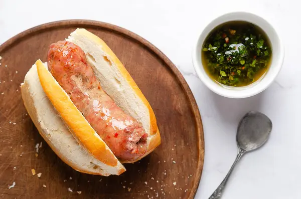 Tahtada bir koripan, chimichurri ile bir kase ve beyaz mermer arka planda bir kaşık. 