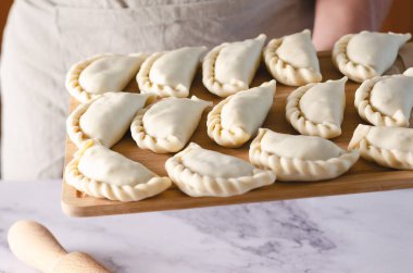 Pişmemiş Arjantin böreğiyle ahşap bir tahtayı tutan bir insan eli..