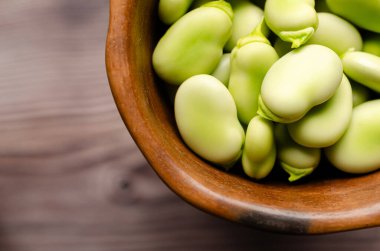 Fresh fava beans in a clay bowl on a wooden background. clipart